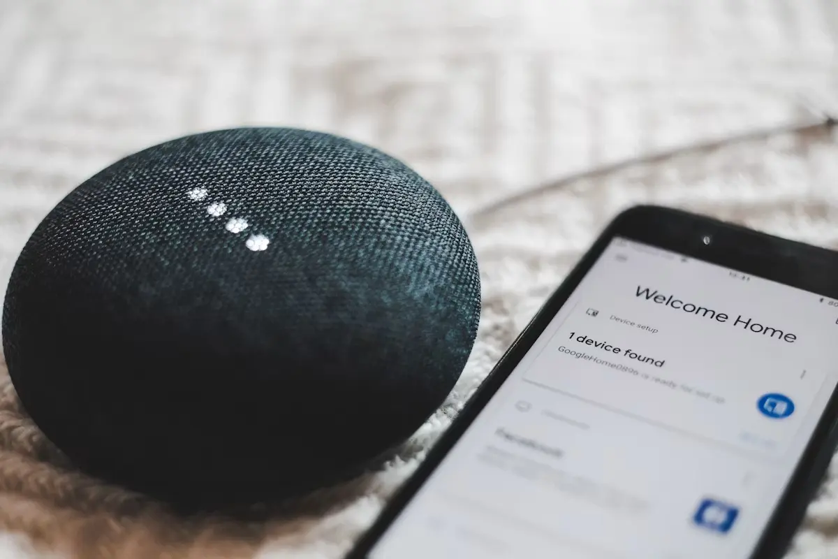A smart speaker assistant device lit up beside a smartphone